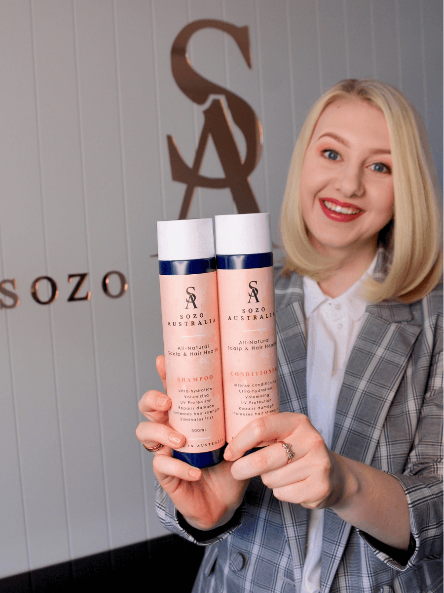 Founder of Sozo Australia, woman with short, blonde hair, holding Sozo Hair Health shampoo and conditioner bottles